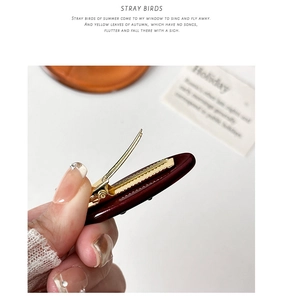 Detailed side view of dark red acetate hair clip showing the sturdy golden metal spring mechanism