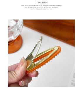 Detail of elegant orange pearlescent hair clip with pearl edges and gold metal duckbill base