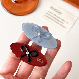 Oval acetate hair clips with crystal bows and gold labels in blue and red colors