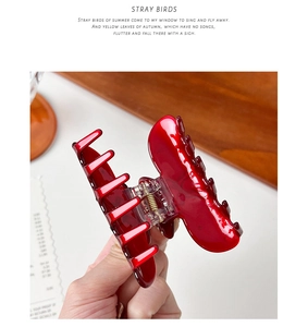 Close-up of a glossy deep red acetate hair claw clip with a strong metal spring detail
