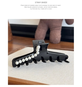 Detail of elegant black acetate hair claw clip featuring polished white faux pearl embellishments