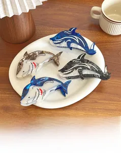 Dettaglio di quattro mollette per capelli a forma di squalo in acetato blu e marrone su un piatto