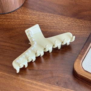 Elegant beige acetate hair claw clip with white pearls on a wooden tray background
