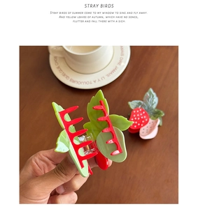 Détail de pinces à cheveux fraise en acétate avec design rouge et vert sur une table en bois