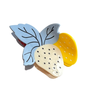Pince à cheveux fraise en acétate avec baie crème et feuille bleue sur fond blanc pur