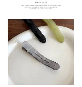 Detailed view of resin duckbill hair clips in grey, black and green on ceramic plate