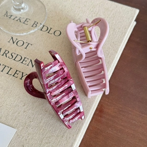 Minimalist heart-shaped claw clips in pink and burgundy on a beige canvas surface