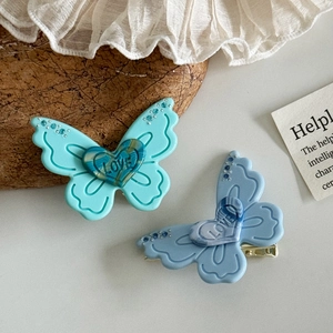 Elegant butterfly hair clips in blue acetate with LOVE heart detail on fabric background