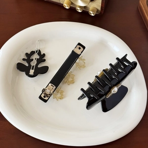 Elegant black hair clip set with pearl reindeer and star accents on white ceramic plate