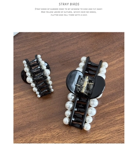 Detail of elegant black resin hair claws with white pearls on a brown wooden background