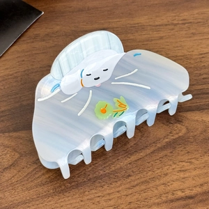 Detail of blue marble claw clip with cute cat face and flower on a wooden table