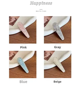 Detail of four textured hair clips in pink, blue, grey, and beige with small rhinestones