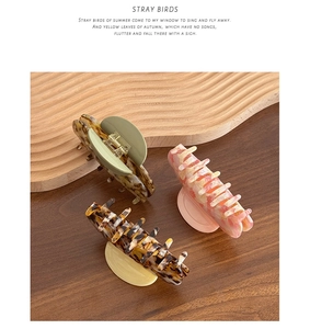 Three acetate hair claws with shell patterns in brown, green, and pink on a wood surface