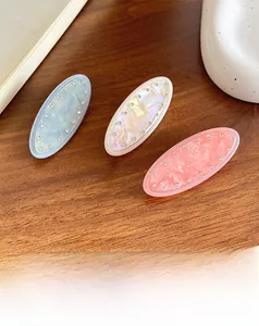 Detail of three oval resin hair clips in blue, white and pink with sparkling rhinestones