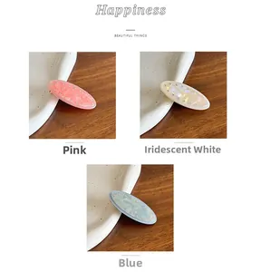 Detail of oval resin hair clips in pink, iridescent white, and blue with rhinestones