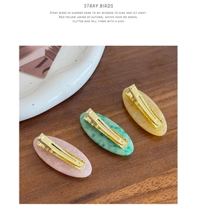 Close-up of three acetate oval hair clips in pink green and amber on a dark wood surface