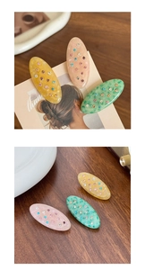 Close-up of three acetate oval hair clips in amber, pink, and green with tiny rhinestones