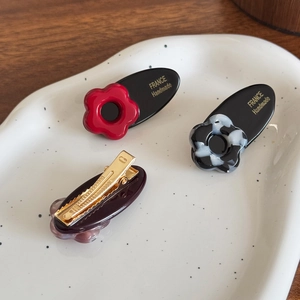 Three-piece acetate floral hair clips set in red, marble, and coffee on a ceramic tray
