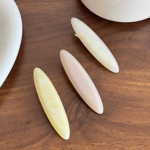 Three elegant acetate marble hair clips in cream, pink and yellow on wooden desk