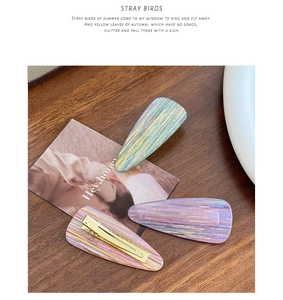 Detail of three colorful acetate hair clips with gradient texture on a wooden surface