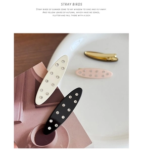 Detailed view of acetate hair clips with rhinestones in four elegant colors on white ceramic