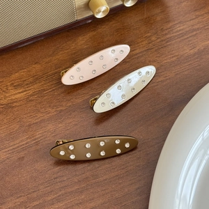 Three acetate duckbill hair clips with rhinestones in pink, cream, and brown on wood