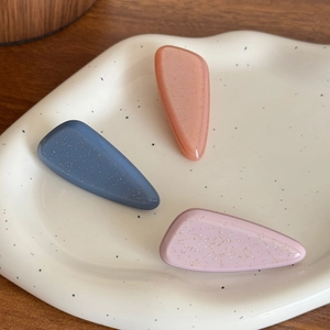 Three glittery acetate teardrop hair clips in blue, pink, and purple on a white tray