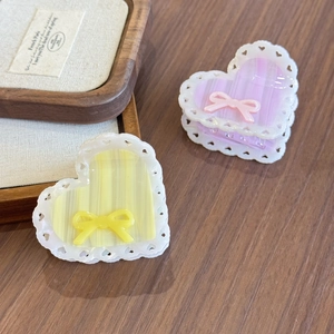 Pink and yellow acetate heart hair claws with lace edges and bows on wooden background