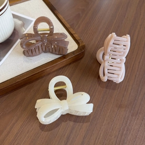 Three jelly-colored bow hair claws in brown, cream, and pink on a warm wooden background