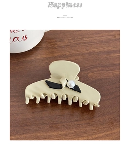 Detail of French resin hair claw clip with bow decoration and pearl on wooden surface