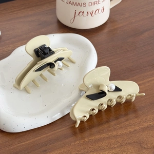 Elegant cream pearl hair claw clip set with black bow detail on a ceramic plate