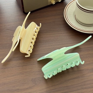 Oversized acetate hair claws in cream and mint green with marble texture on wood surface