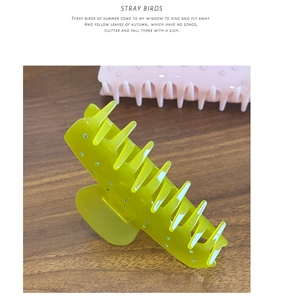 Detail showing neon yellow resin hair claw clip with sparkling rhinestones on wood