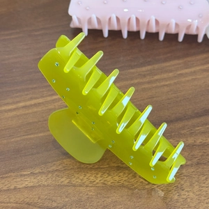 Neon yellow acetate shark hair claw clip with rhinestones on dark wood background