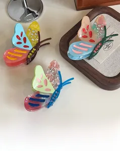 Detailed view of three acetate butterfly hair claws with colorful rhinestones on wood tray