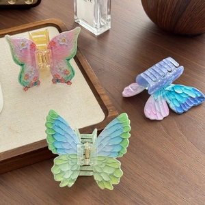 Vibrant butterfly hair claws in colorful acrylic floral and gradient styles on a wooden tray