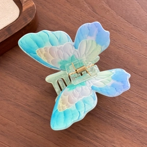 Vibrant butterfly hair claw clip with colorful gradient wings on a natural wood surface