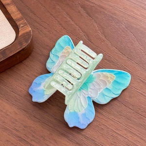 Translucent butterfly hair claw clip with blue and green gradient on a wooden background