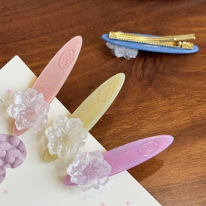 Set of four pastel camellia acetate hair clips with glitter finish on a wooden background
