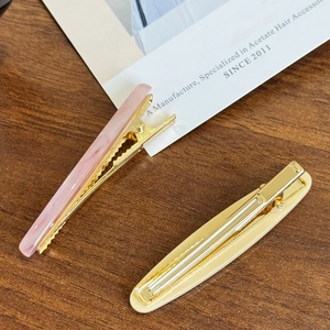Elegant oval acetate hair clips in pink marble and cream beige on a wood surface