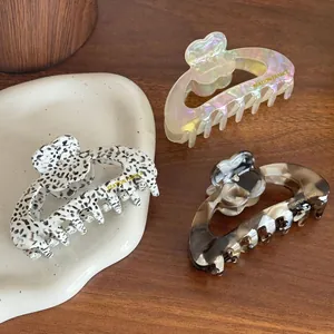 Three premium acetate hair claws with flower patterns and diamond accents on a tray