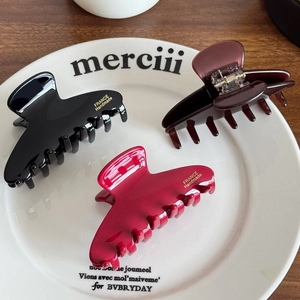 Three acetate shark hair clips in black and red tones with gold branding on a white tray