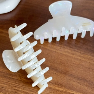 Elegant ivory and pearlescent acetate hair claws with gold metal labels on wood