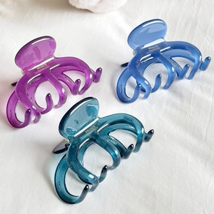Three premium acetate hair claws in purple, royal blue, and teal on white fabric