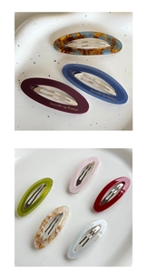 Détail de barrettes ovales colorées en acétate avec logo doré sur plateau blanc