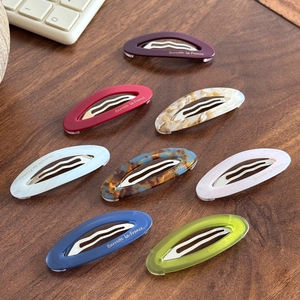 Barrettes ovales colorées en acétate avec logo doré sur fond de bureau en bois naturel