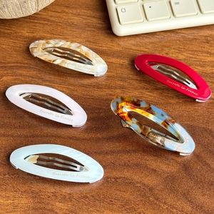 Lot de 5 barrettes ovales en acétate avec étiquette dorée sur surface bois foncée