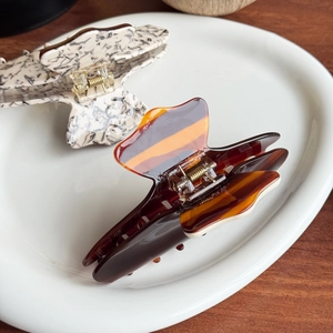 Colorful striped acetate hair claw clips in amber and marble finish on a white plate