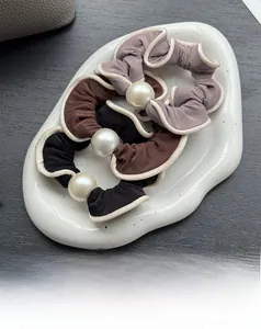 Close-up of three pearl elastic hair scrunchies in black, brown, and purple on a white tray