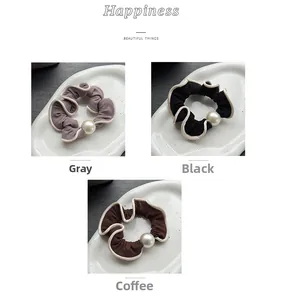 Three pleated pearl hair scrunchies in grey, black, and coffee colors on ceramic plates